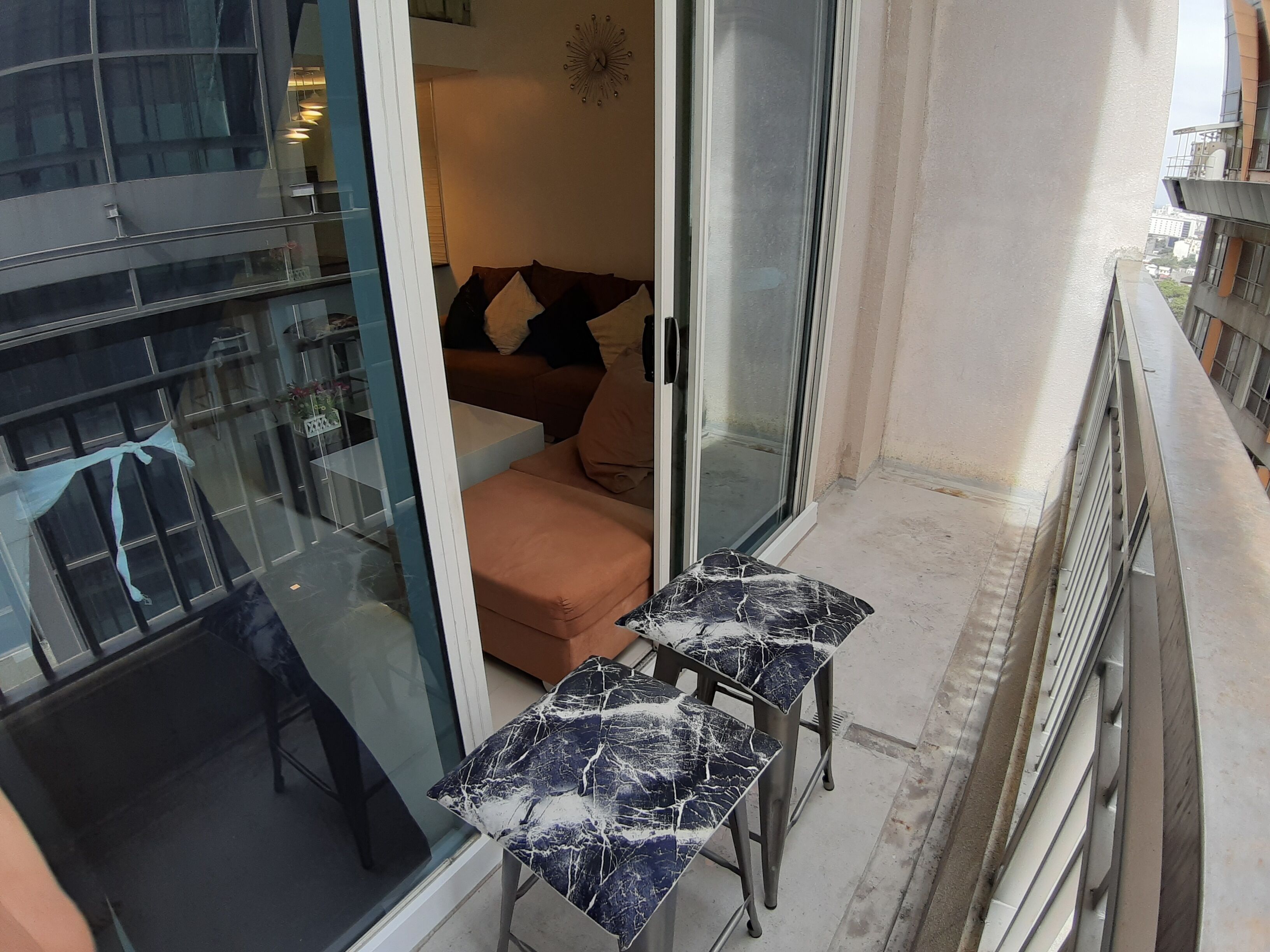 A balcony with a glass door leading to a living area, a small table, and a sofa with cushions.