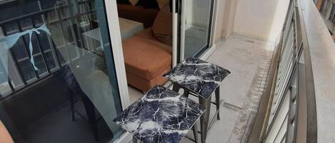 A balcony with a glass door leading to a living area, a small table, and a sofa with cushions.