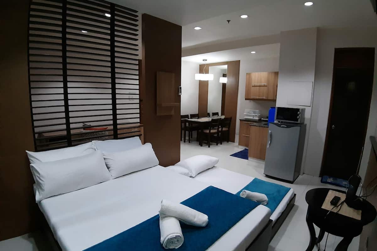 A hotel room with a bed, a desk, a chair, a kitchenette, and a bathroom.