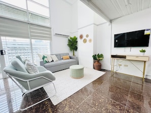 A modern living room with a grey sofa, a white armchair, a TV, and a small plant on a console table.