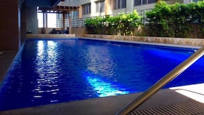An indoor swimming pool with clear blue water, surrounded by a building with multiple windows and a covered area with plants. - Luxury Loft in Cebu City (Cebu City)
