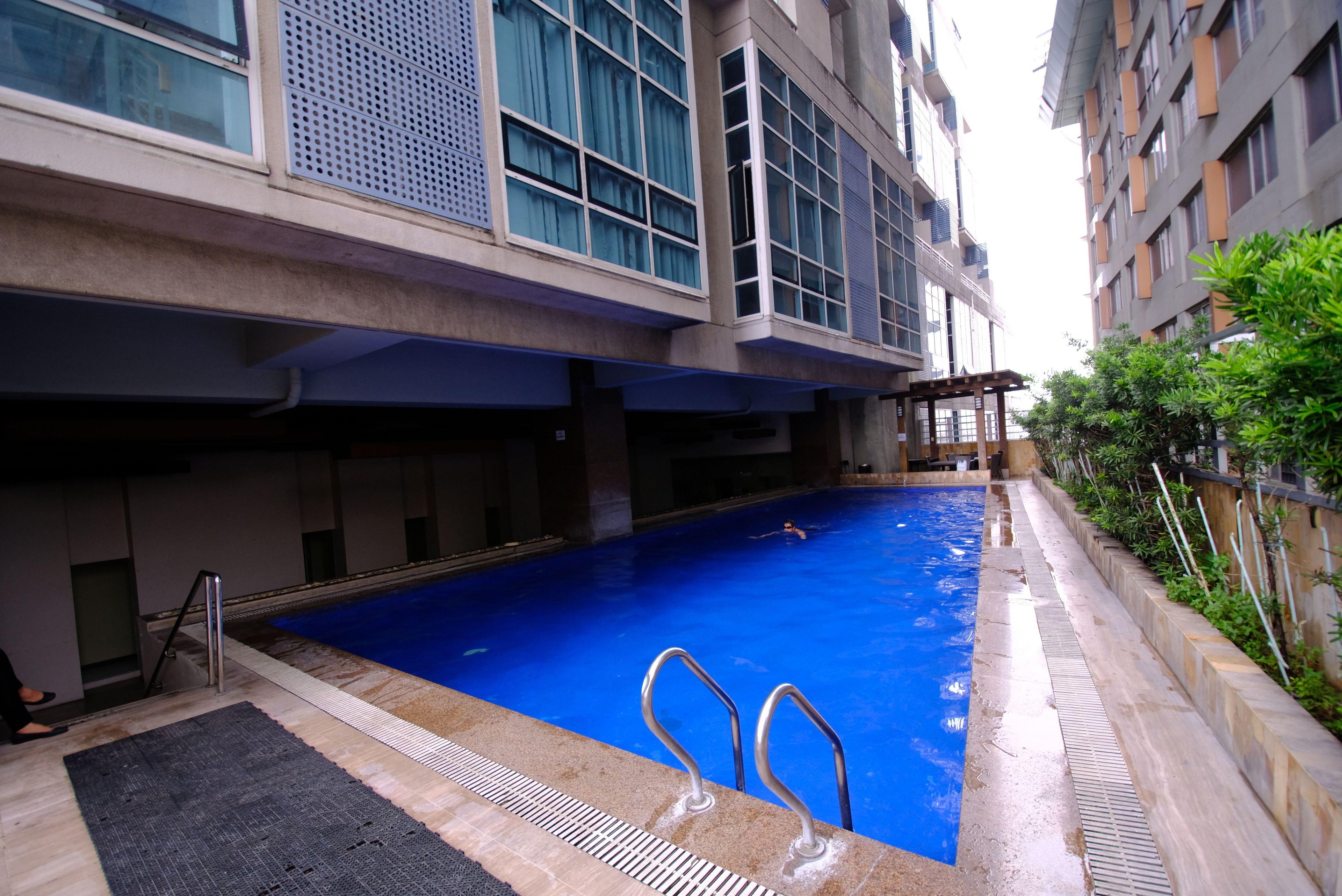 Une piscine intérieure à l’eau d’un bleu limpide, entourée d’un bâtiment moderne doté de grandes fenêtres et d’une allée carrelée.