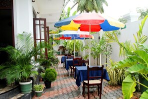 A covered outdoor seating area with tables and chairs, surrounded by potted plants. - Hotel Italia (Ambalangoda)