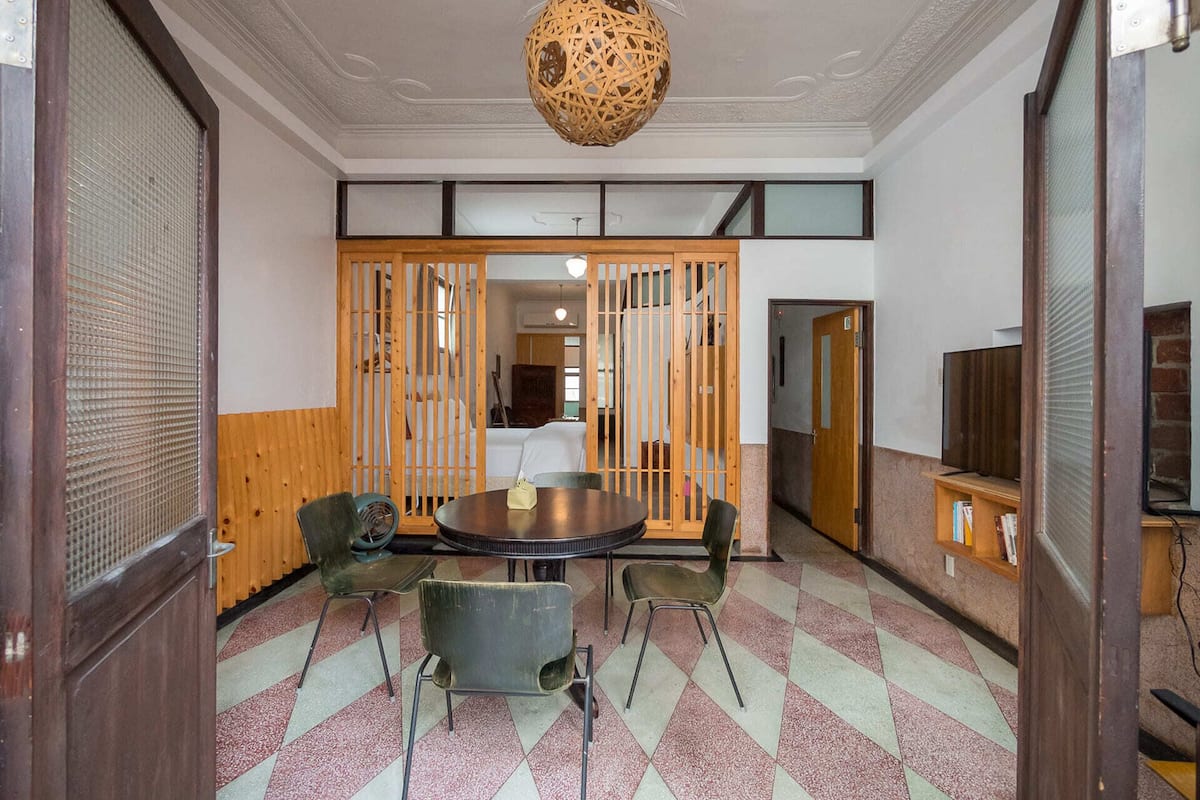 A room with a round table, four chairs, a woven ceiling light, and a wooden partition.