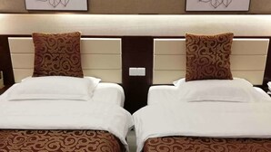 Une chambre d’hôtel avec deux lits simples, chacun agrémenté d’une couvre-lit à motifs et de coussins assortis. La chambre est dotée d’une tête de lit avec un panneau décoratif et de deux œuvres d’art florales fixées au mur.