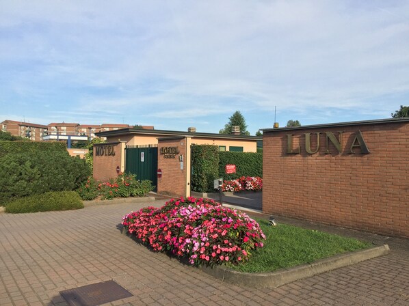 A hotel entrance with a brick facade, a green gate, and a flower bed with pink flowers.