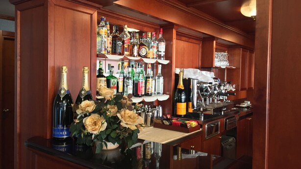 A bar area with wooden paneling, a variety of liquor bottles, a wine cooler, and a flower arrangement. - Hotel Motel Luna (Segrate)