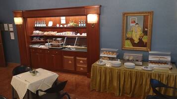 Et morgenmadsområde med buffet, borde, stole og et billede på væggen.