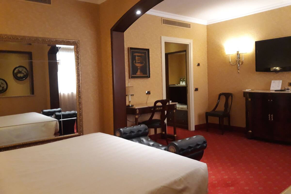 A hotel room with a bed, a desk, a chair, a television, and a wardrobe.