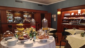 A buffet setup with various food items and beverages, a bar area with liquor bottles, and neatly arranged tables with chairs. - Hotel Motel Luna (Segrate)