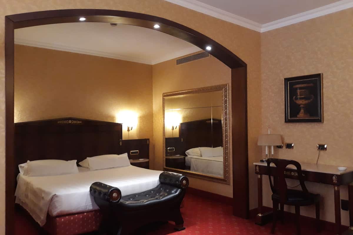 A hotel room with a large bed, a desk, a chair, a mirror, and a framed picture on the wall.