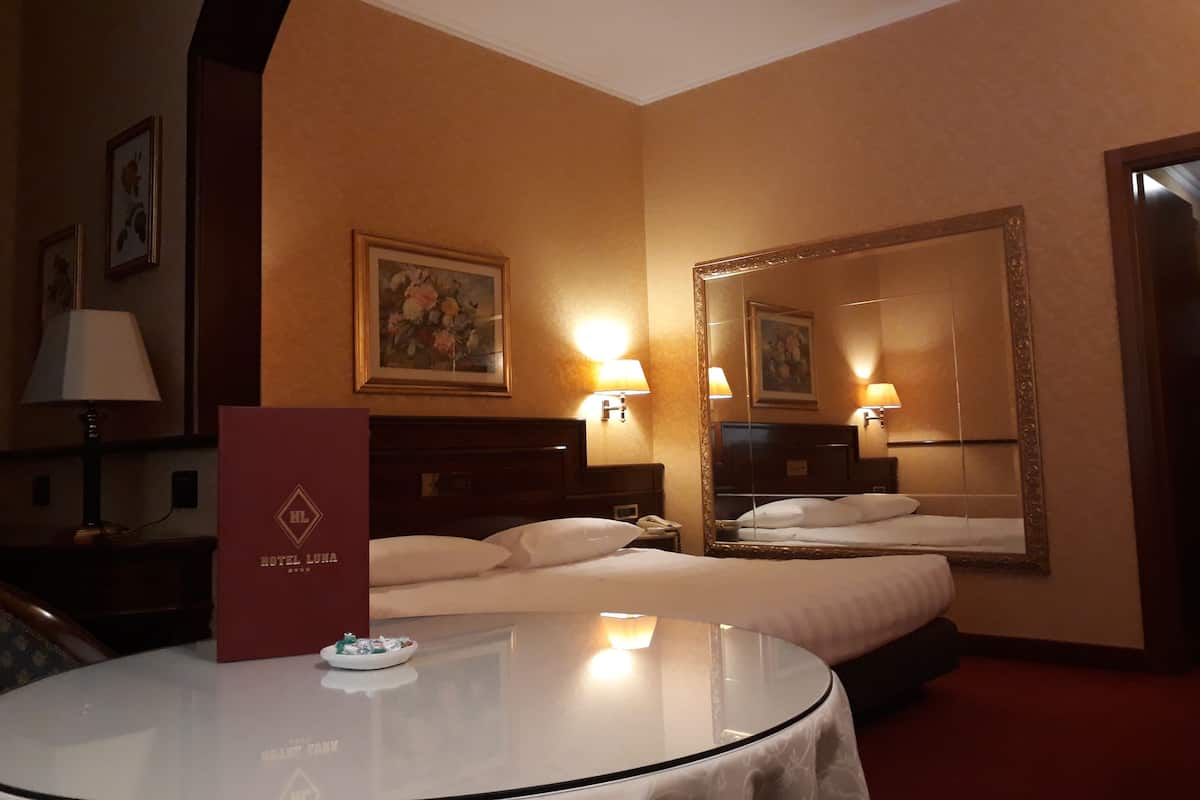 A hotel room with a bed, a round table with a tray of snacks, a mirror, and a framed picture on the wall.