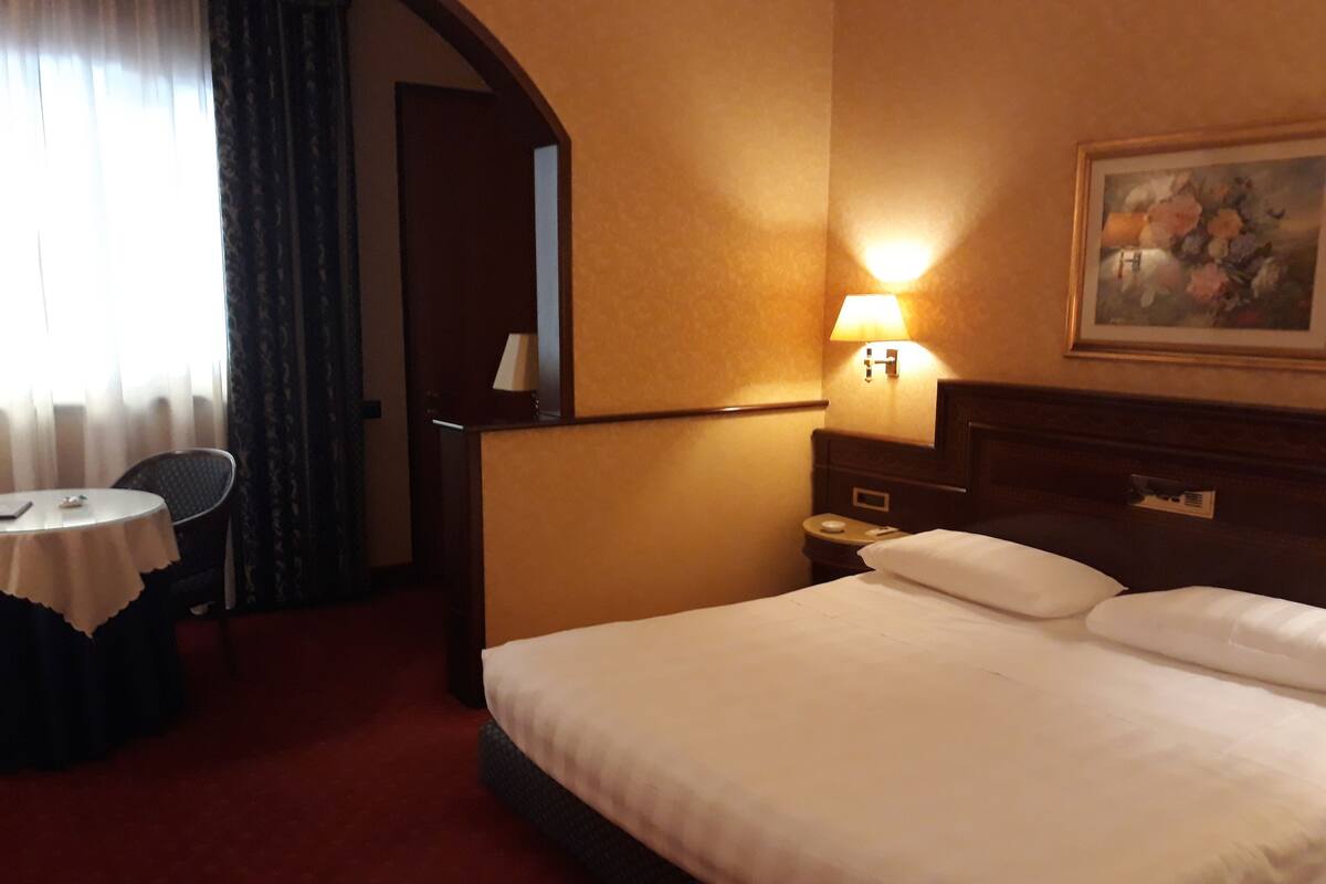 A hotel room with a bed, a nightstand, a lamp, a chair, and a table.