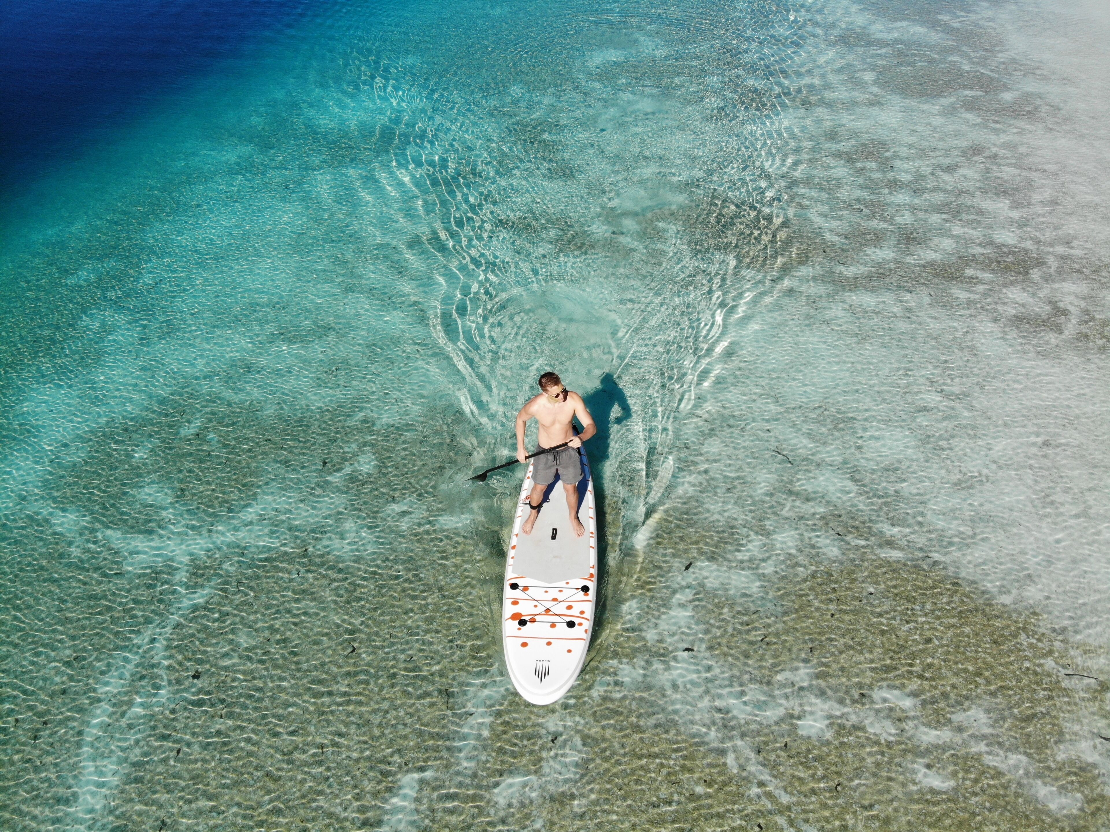 Una persona haciendo paddleboard en aguas turquesas cristalinas con un barco.