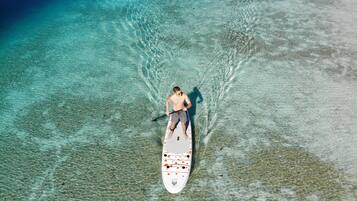 Una persona haciendo paddleboard en aguas turquesas cristalinas con un barco.