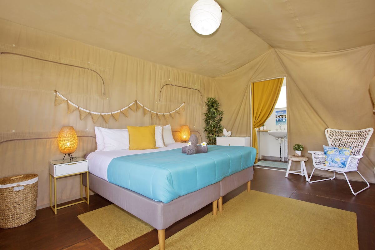 A bedroom with a bed, bedside lamps, a chair, a small table, and a plant.