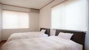 A room with two beds, a window with blinds, an air conditioning unit, and a wooden floor. - Guesthouse ILOHA (Kyoto)
