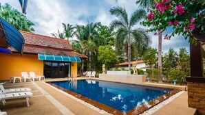 Una piscina con sillones de descanso y un edificio con tejado de baldosas.
