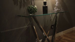 A glass console table with a vase of white flowers, a black candle holder, and a modern lamp. - K Rooms (Rome)