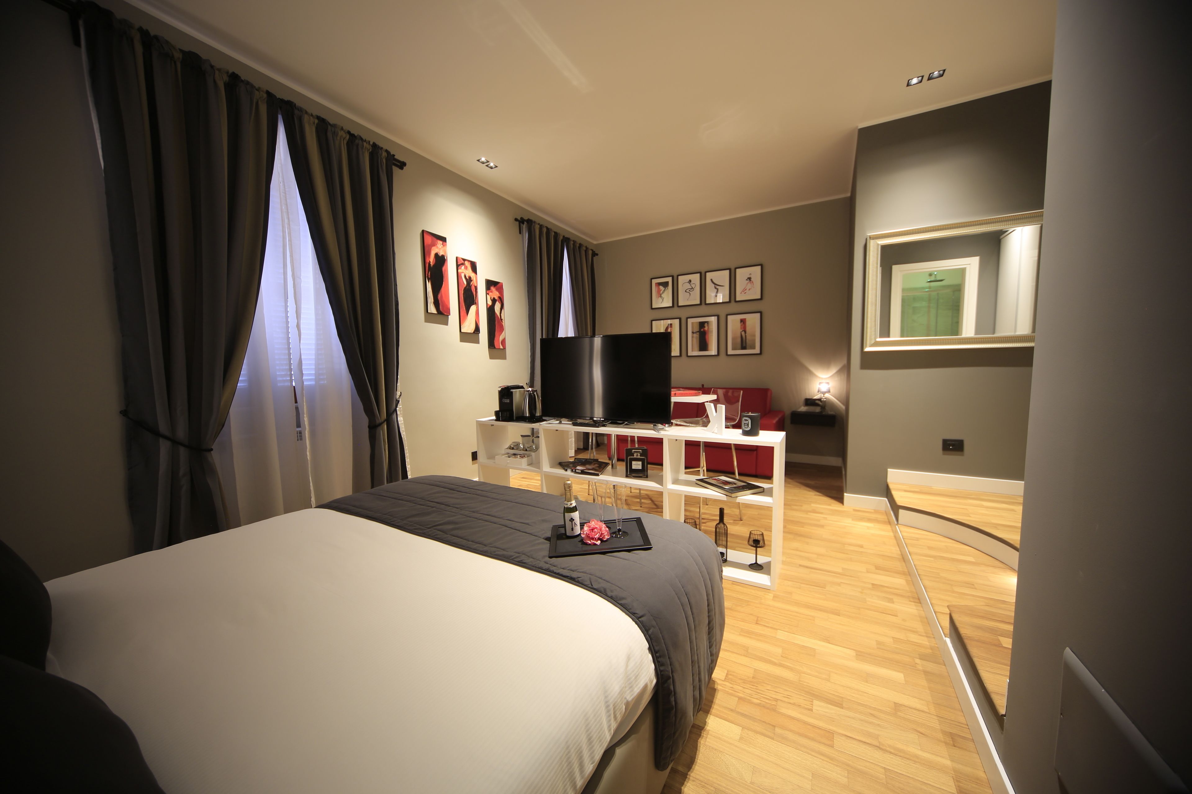 A hotel room with a bed, a TV, a desk with a computer, and a bookshelf.