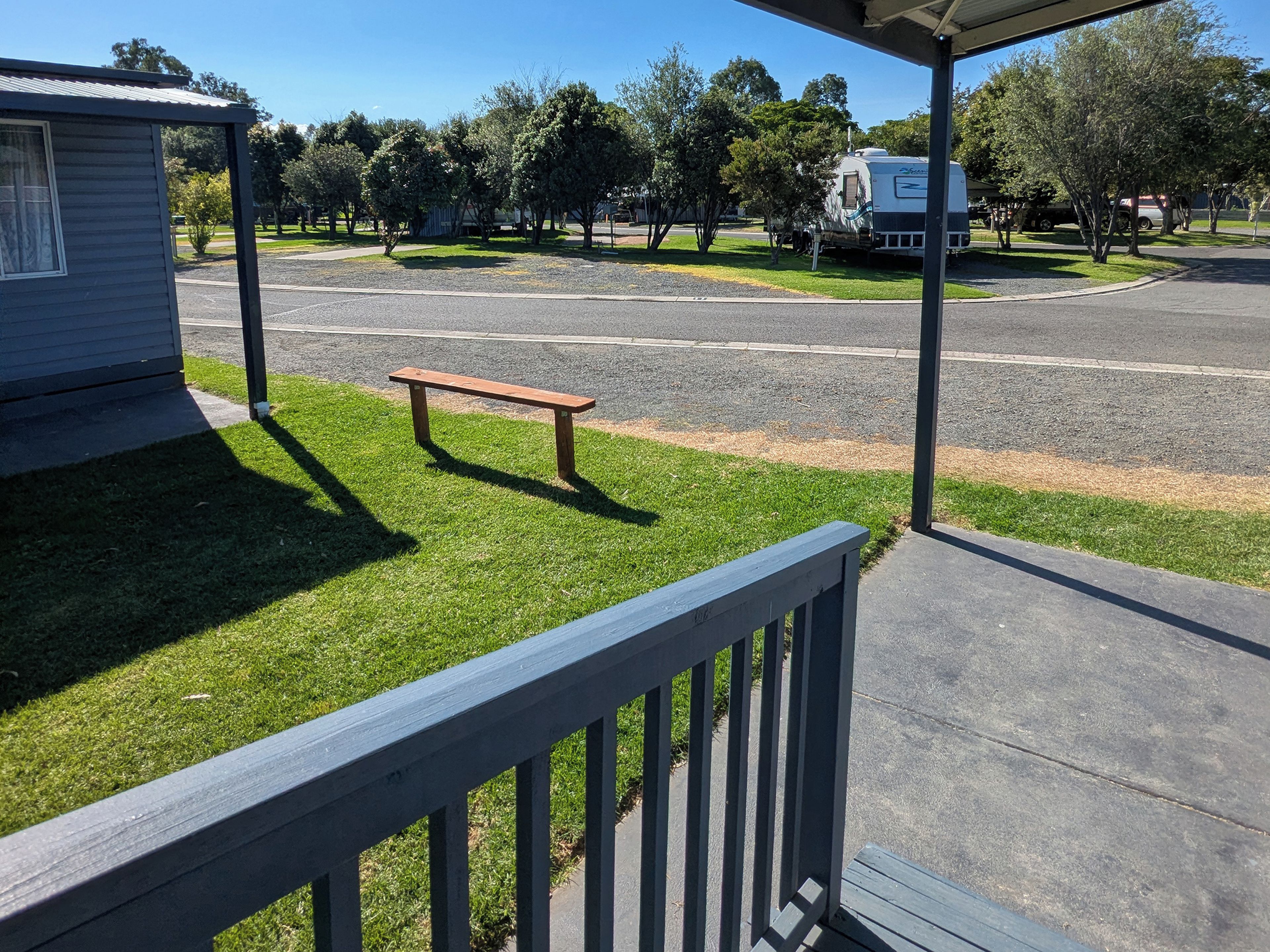 A grassy area with a bench, a paved road, and a parked RV.