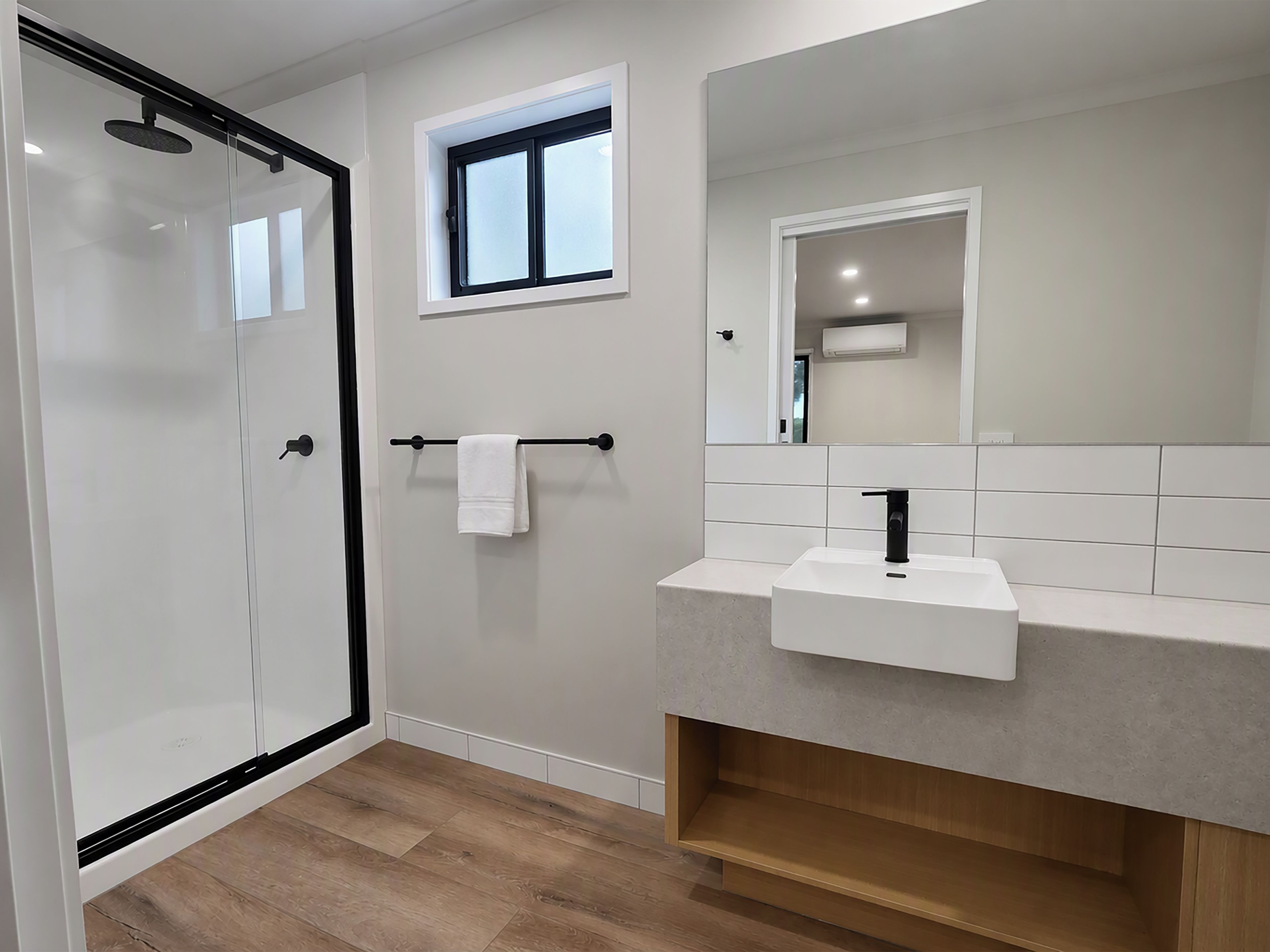 A modern bathroom with a glass shower enclosure, a white sink, and a small window above the mirror.