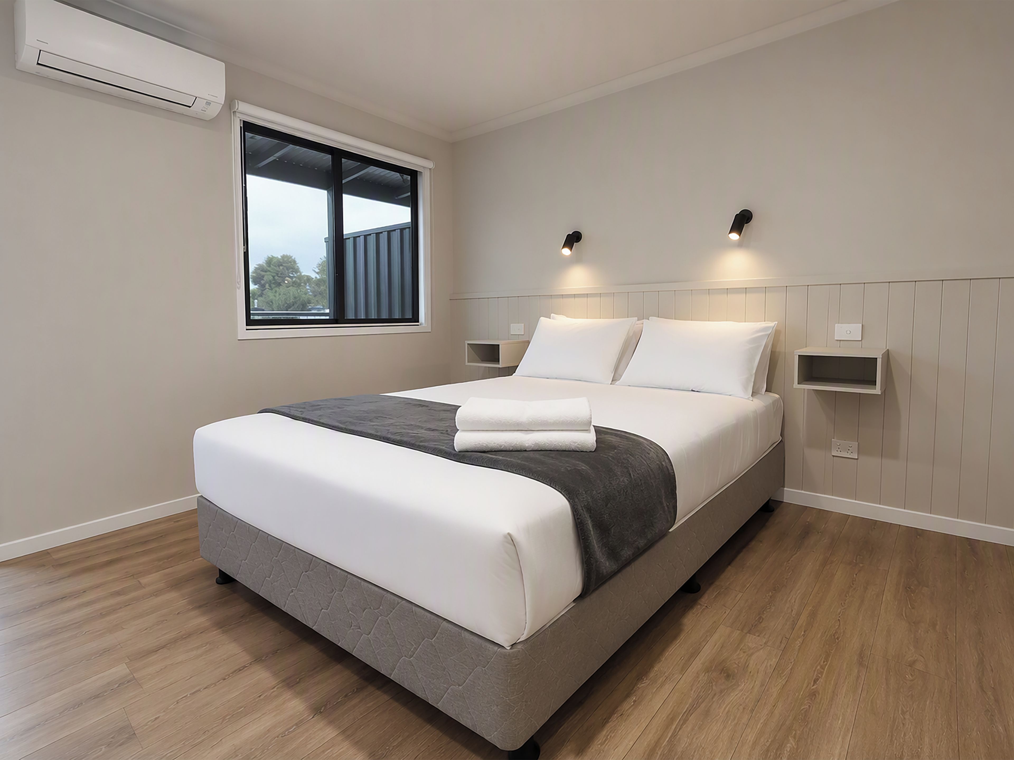 A modern bedroom with a large bed, a window, and built-in wall lighting.