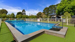 A rectangular swimming pool with a surrounding white fence, a small gazebo, and a grassy area with trees in the background. - Traralgon Holiday Village (Traralgon)