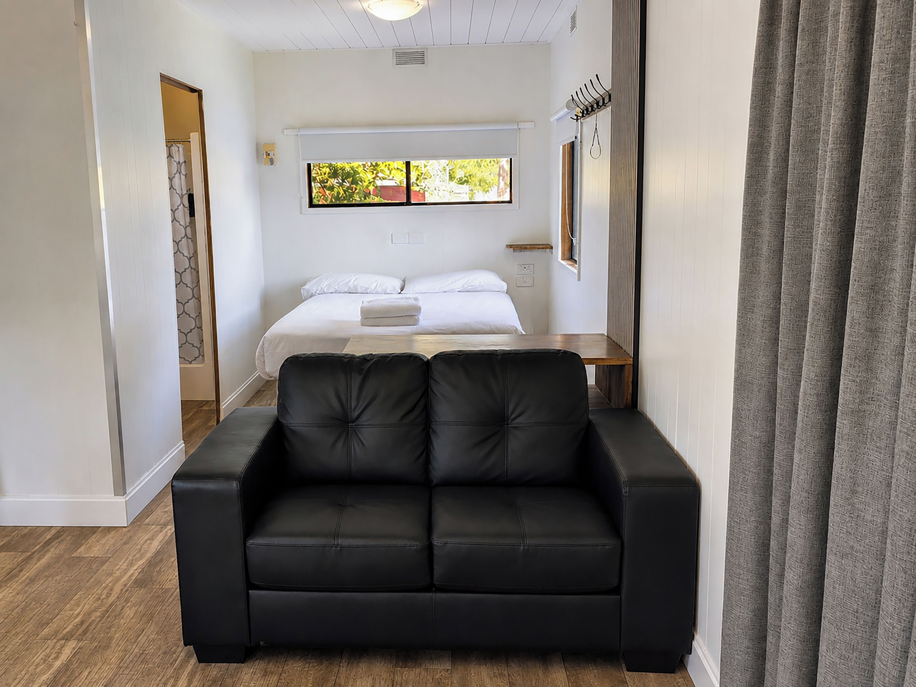 A hotel room with a bed, a black leather sofa, a window with a view, and a coat rack.