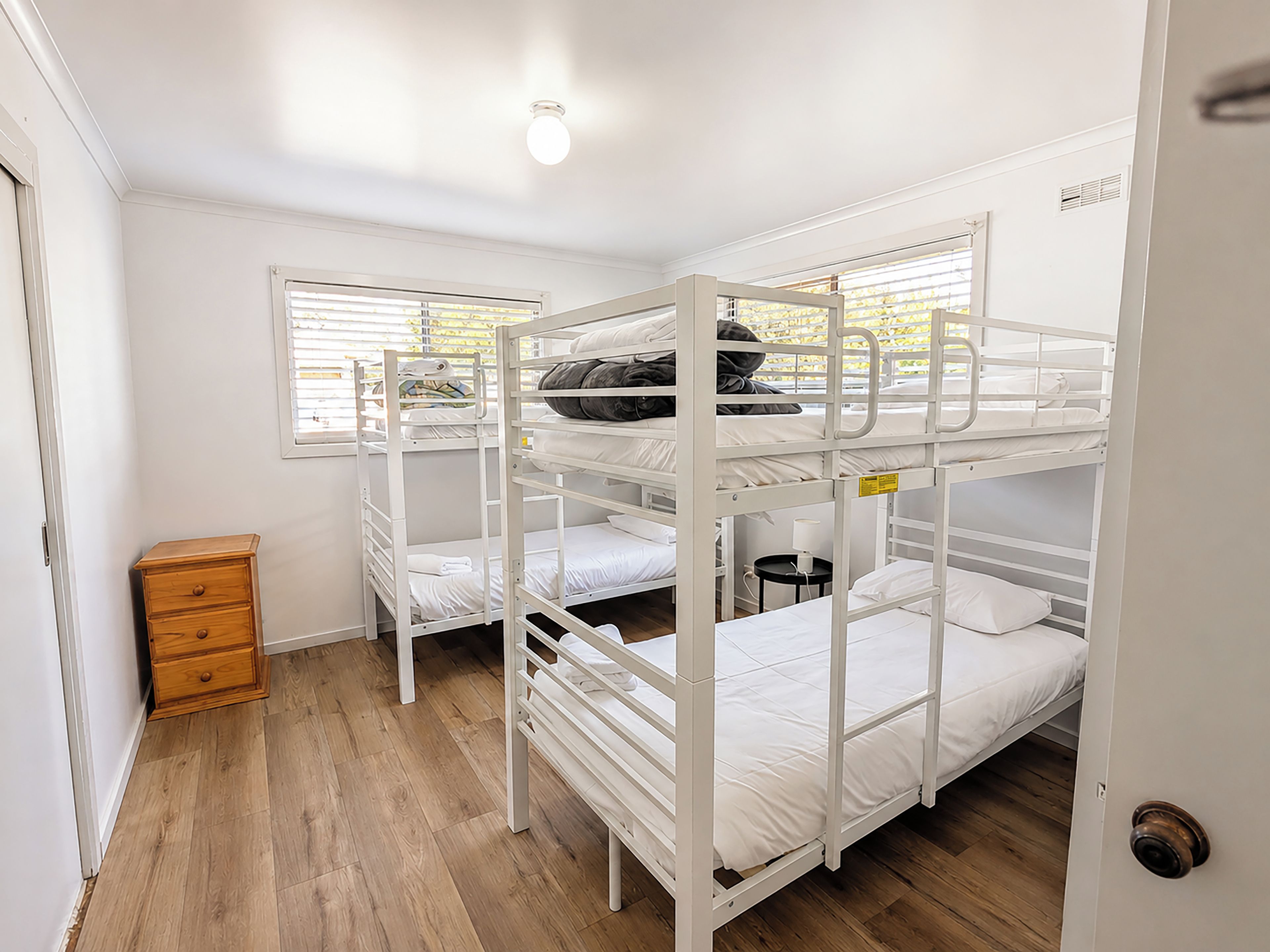 A bunk room with three bunk beds, a wooden dresser, and a window with blinds.
