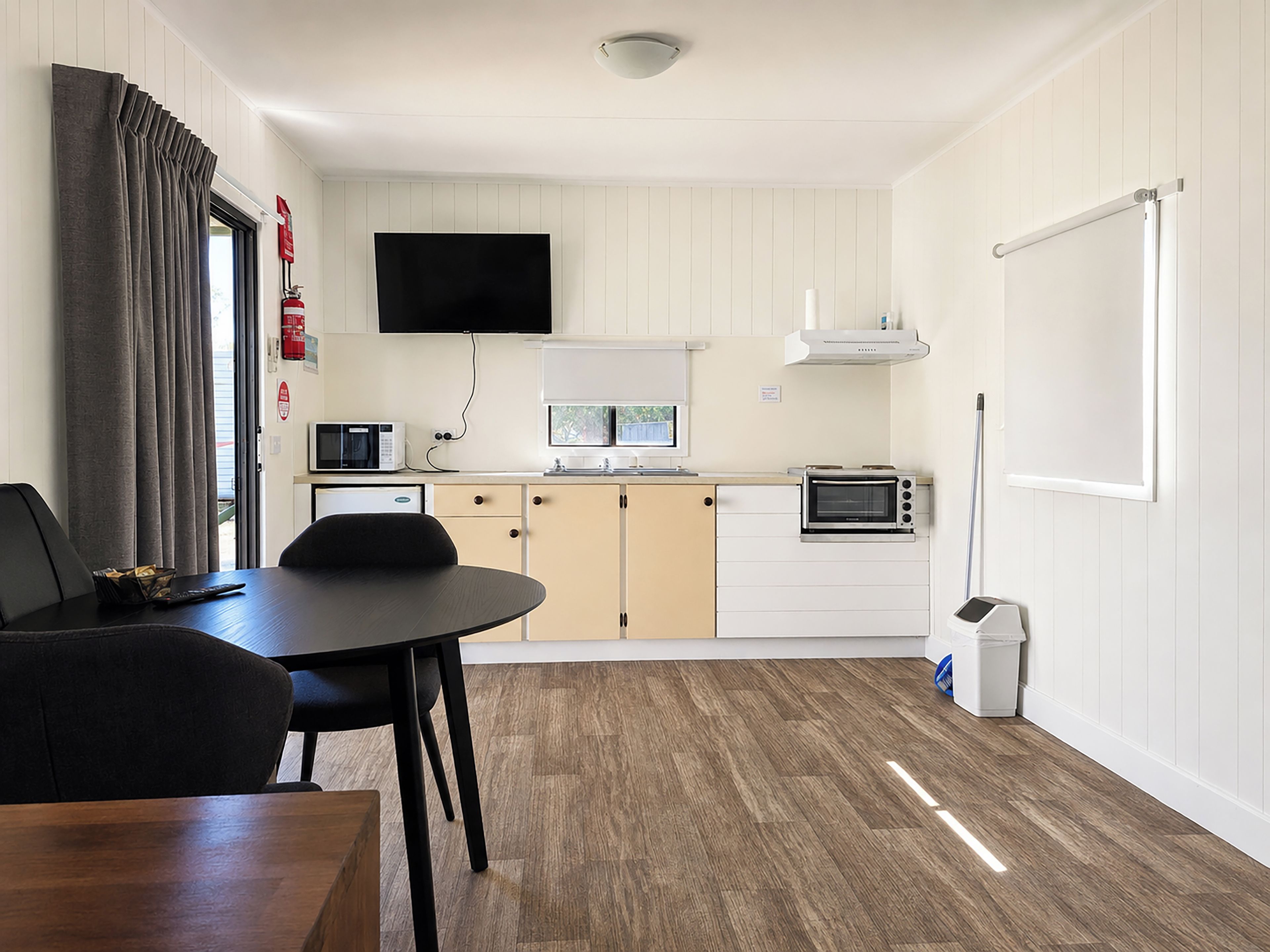 A compact kitchen with a dining table, chairs, a microwave, a toaster, and a television mounted above the counter.