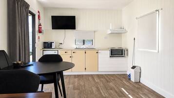 A compact kitchen with a dining table, chairs, a microwave, a toaster, and a television mounted above the counter.
