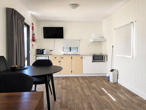 Una cocina compacta con una mesa de comedor, sillas, un microondas, un tostador y un televisor colocado sobre la encimera.