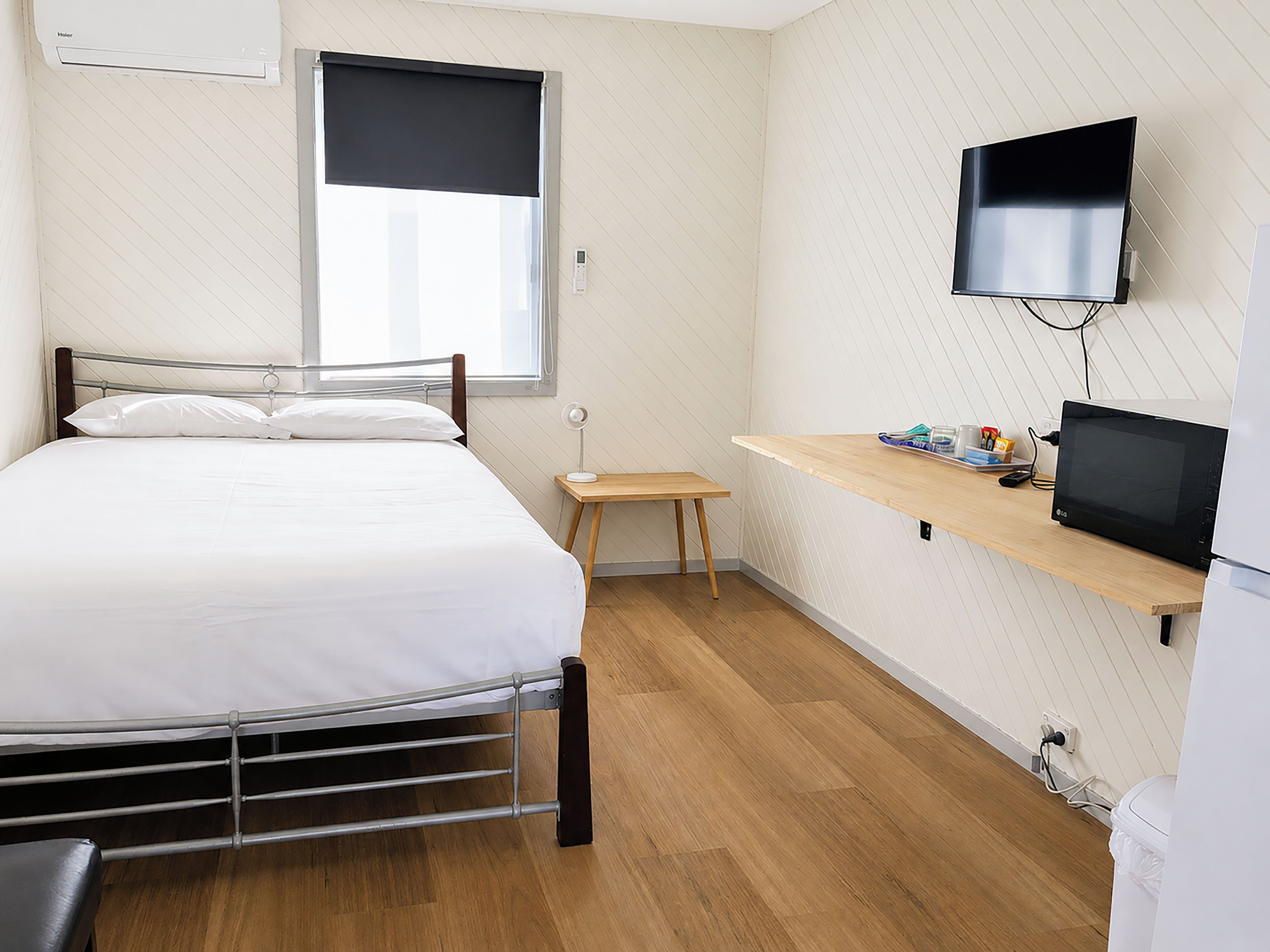 Un dormitorio con cama, mesita de noche, televisor y ventana con persiana.