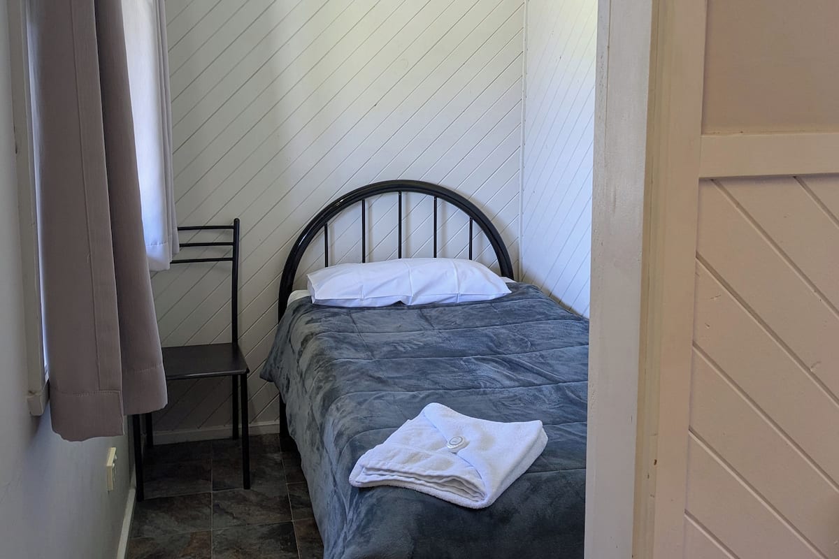 Una habitación pequeña y estrecha con una cama individual, una silla y una puerta.