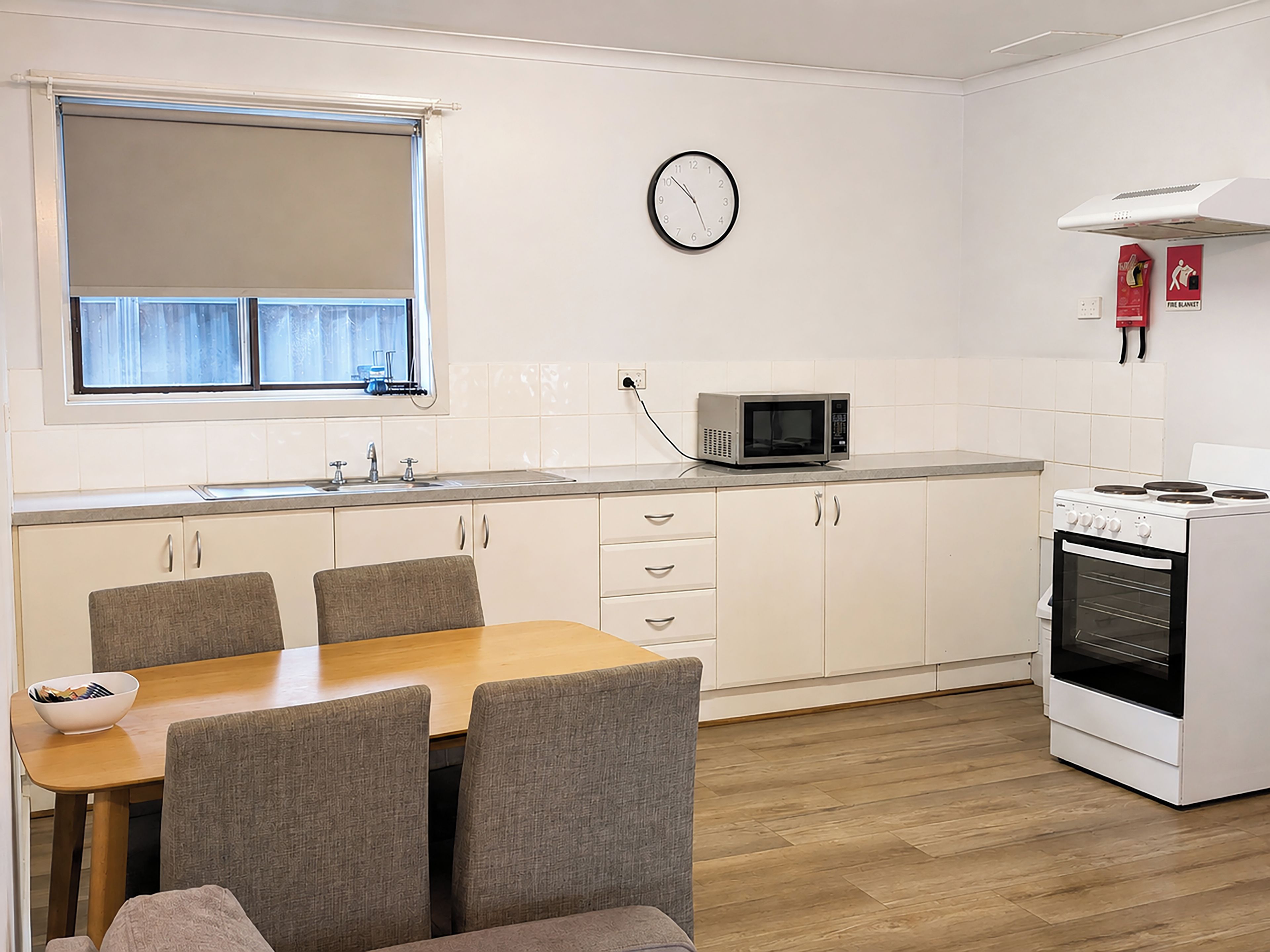Una cocina compacta con una mesa de comedor, sillas, microondas, estufa y un reloj en la pared.