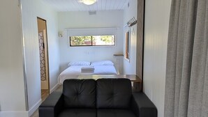 A room with a black sofa, a bed with white linens, a window with a view, and a coat rack. - Traralgon Holiday Village (Traralgon)