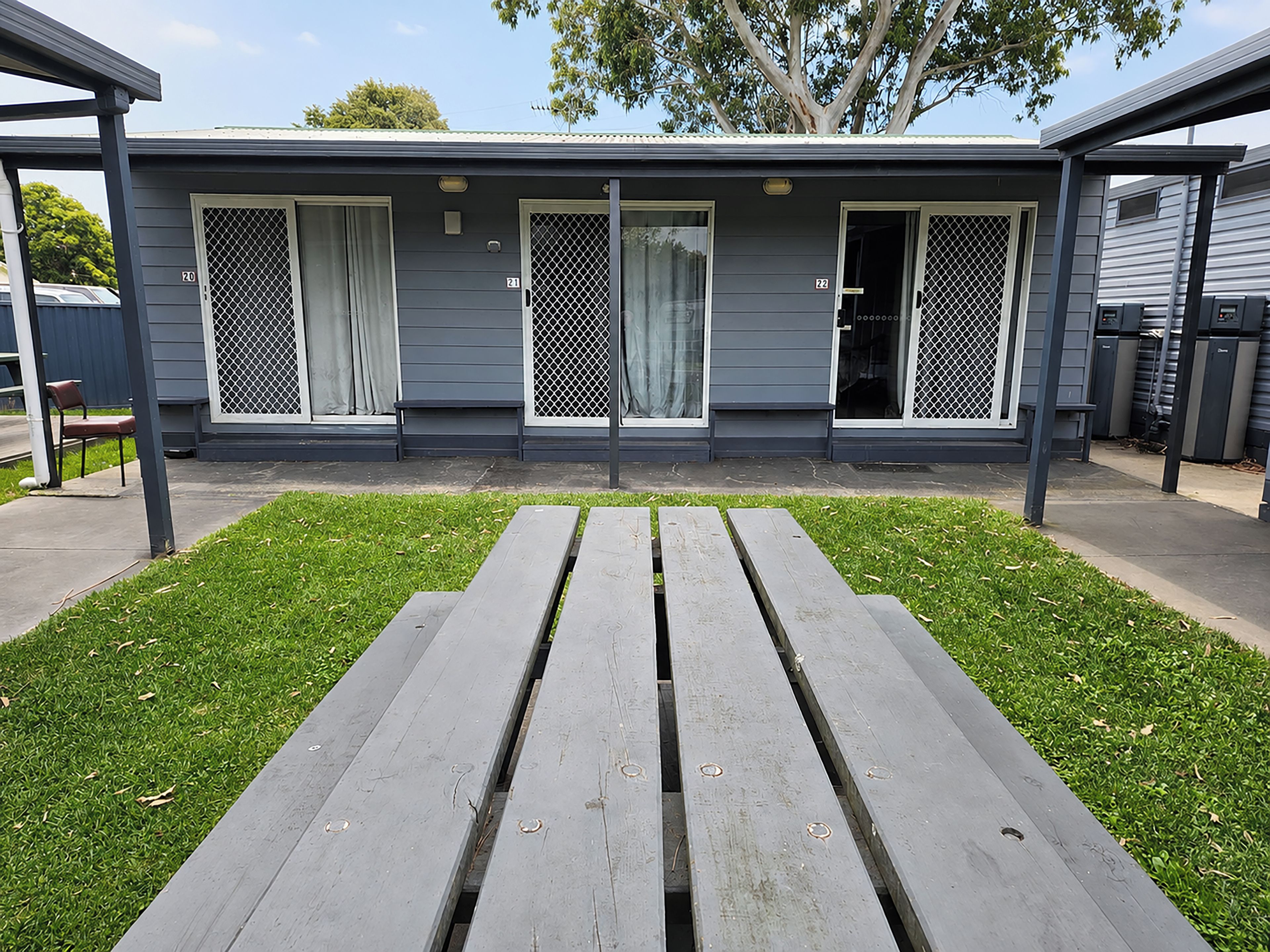 A covered outdoor area with a picnic table in the foreground and a building with numbered windows in the background.