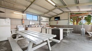A covered outdoor kitchen area with a picnic table, a refrigerator, a microwave, and a sink. - Traralgon Holiday Village (Traralgon)