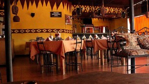 Un restaurant avec des tables et des chaises, un canapé agrémenté de coussins à motifs et une enseigne indiquant « Arusha Backpackers Hotel ».
