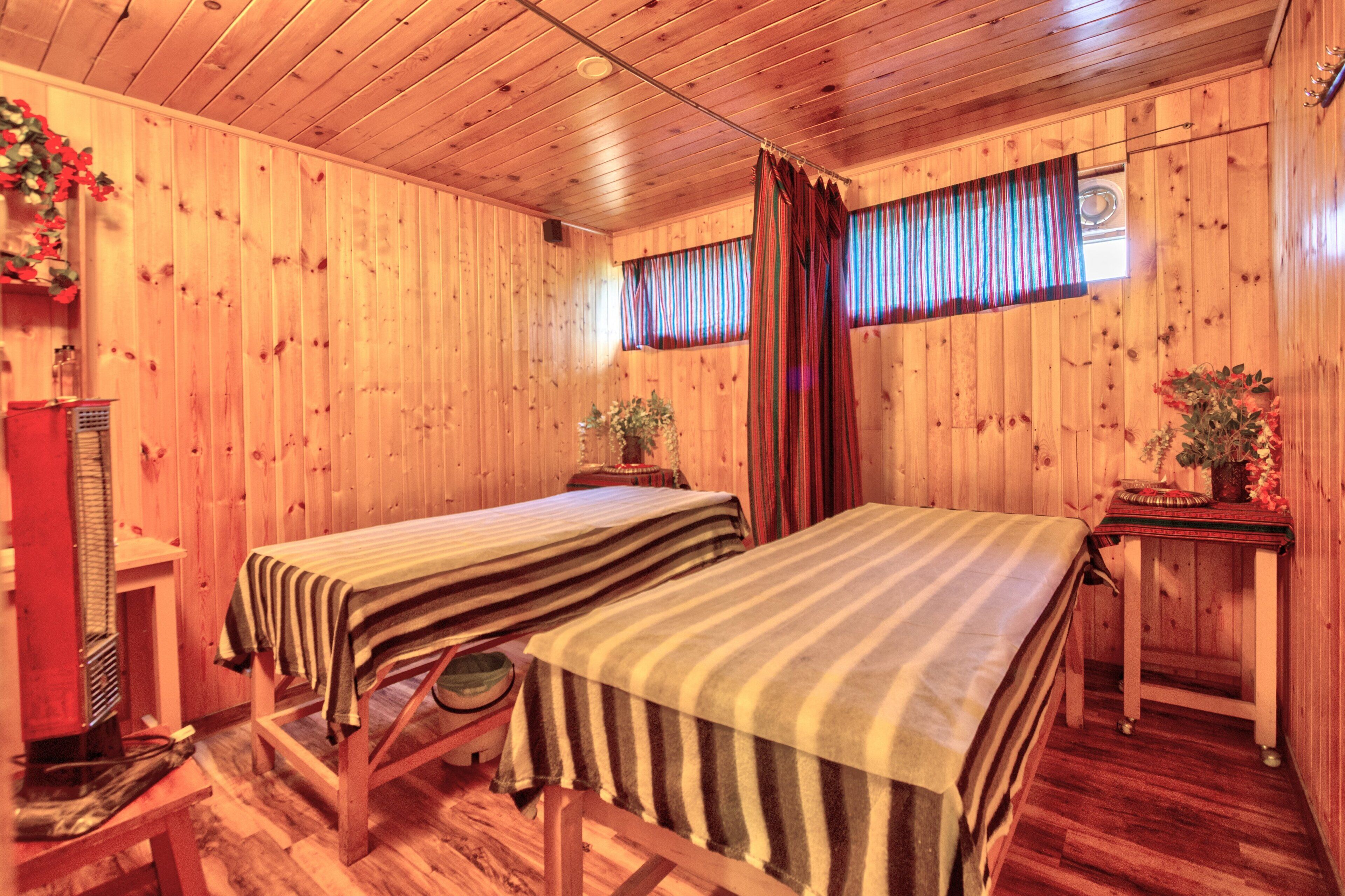 Una habitación con piso de madera, dos camas, una mesita y un armario.
