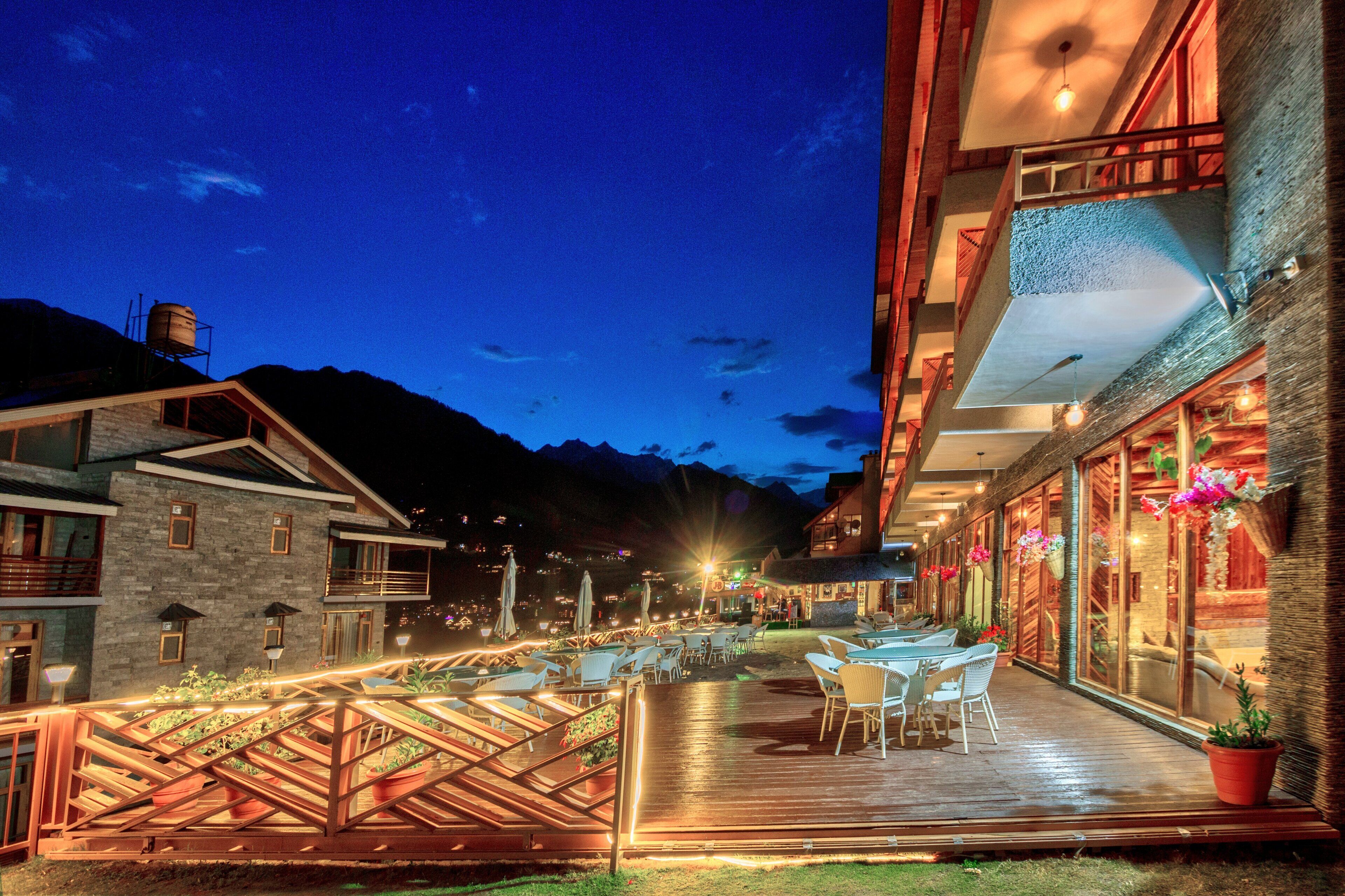 A modern hotel with a wooden deck, outdoor seating, and mountain views.