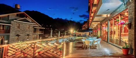 A modern hotel with a wooden deck, outdoor seating, and mountain views.