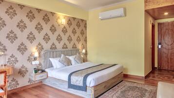 Quarto de hotel com cama, mesas de cabeceira, uma mesa de centro de vidro com itens de café da manhã, porta de madeira e papel de parede estampado.