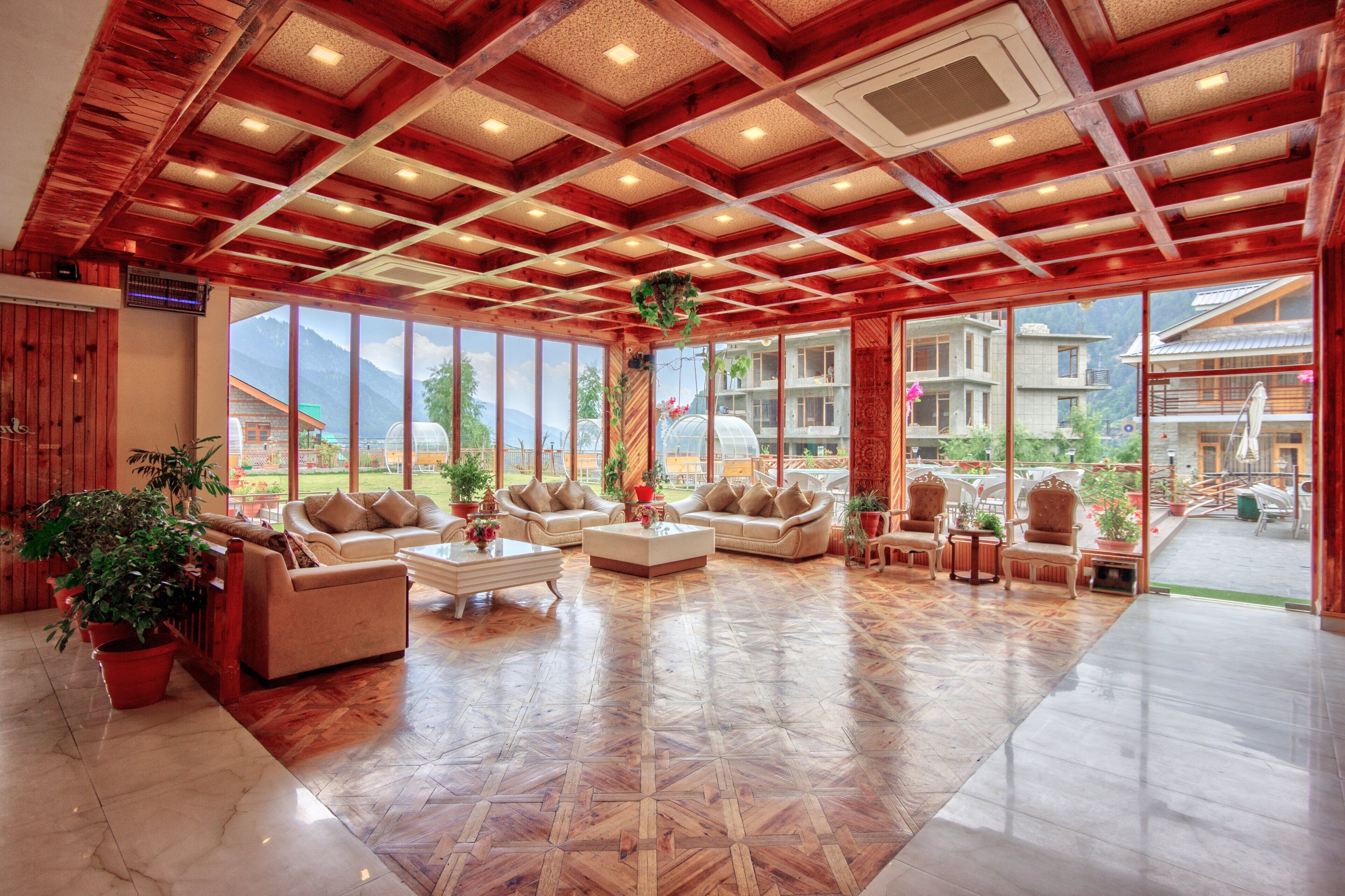 A spacious living area with wooden flooring, large windows, and multiple seating arrangements including sofas and armchairs.
