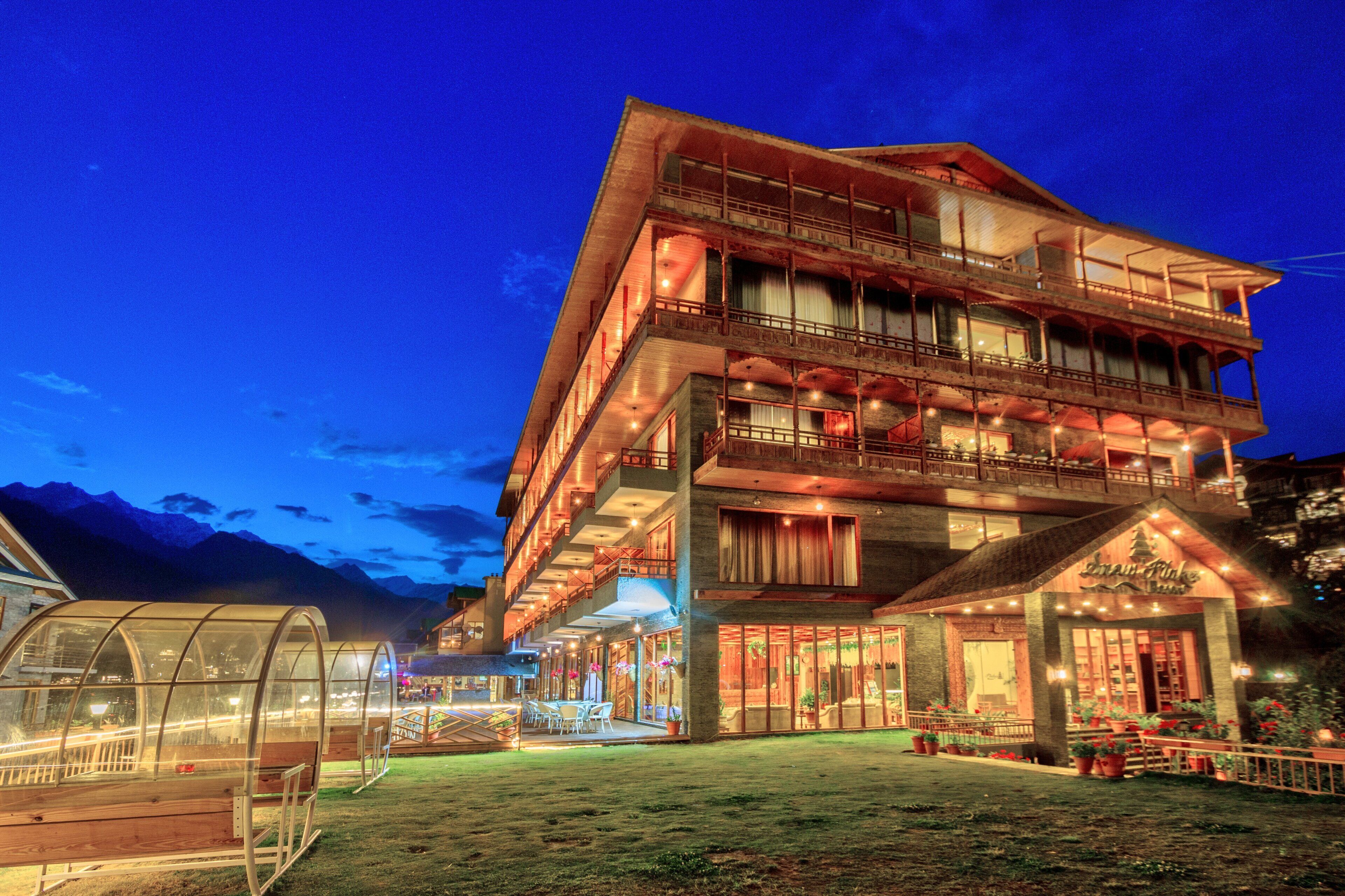 Een meerhoog hotel met een balkon op de bovenste verdieping, een overdekt buitenzitgedeelte en een bord met de naam 'Inn of the Alps'.