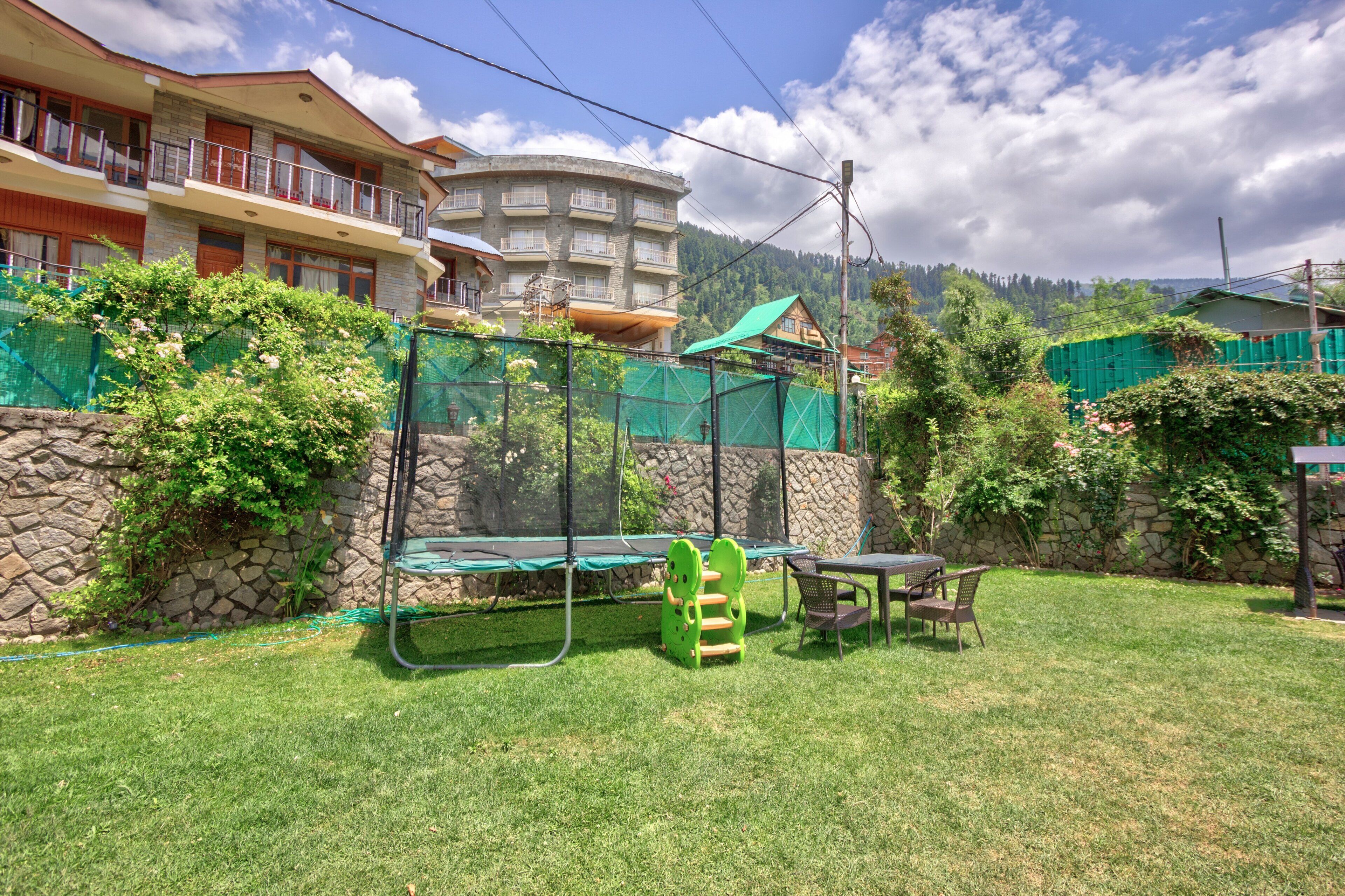 Zona residencial con muro de piedra, un trampolín y una mesa con sillas.