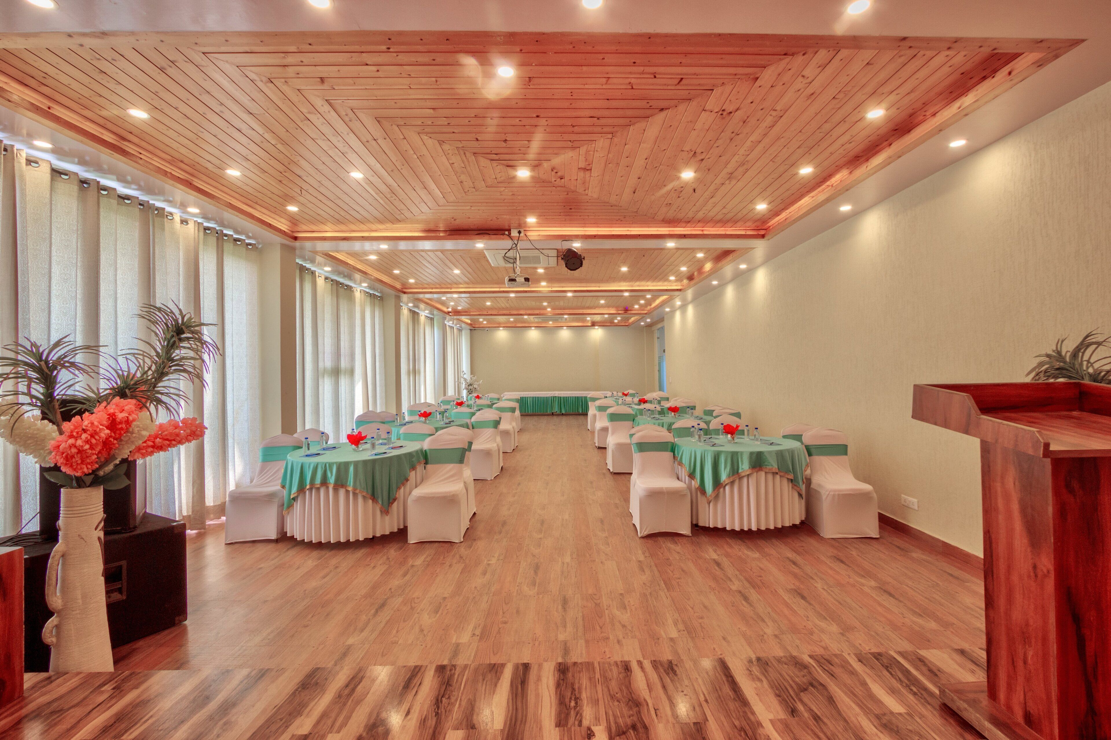 A conference room with wooden floors, green tablecloths, white chairs, and a wooden podium.