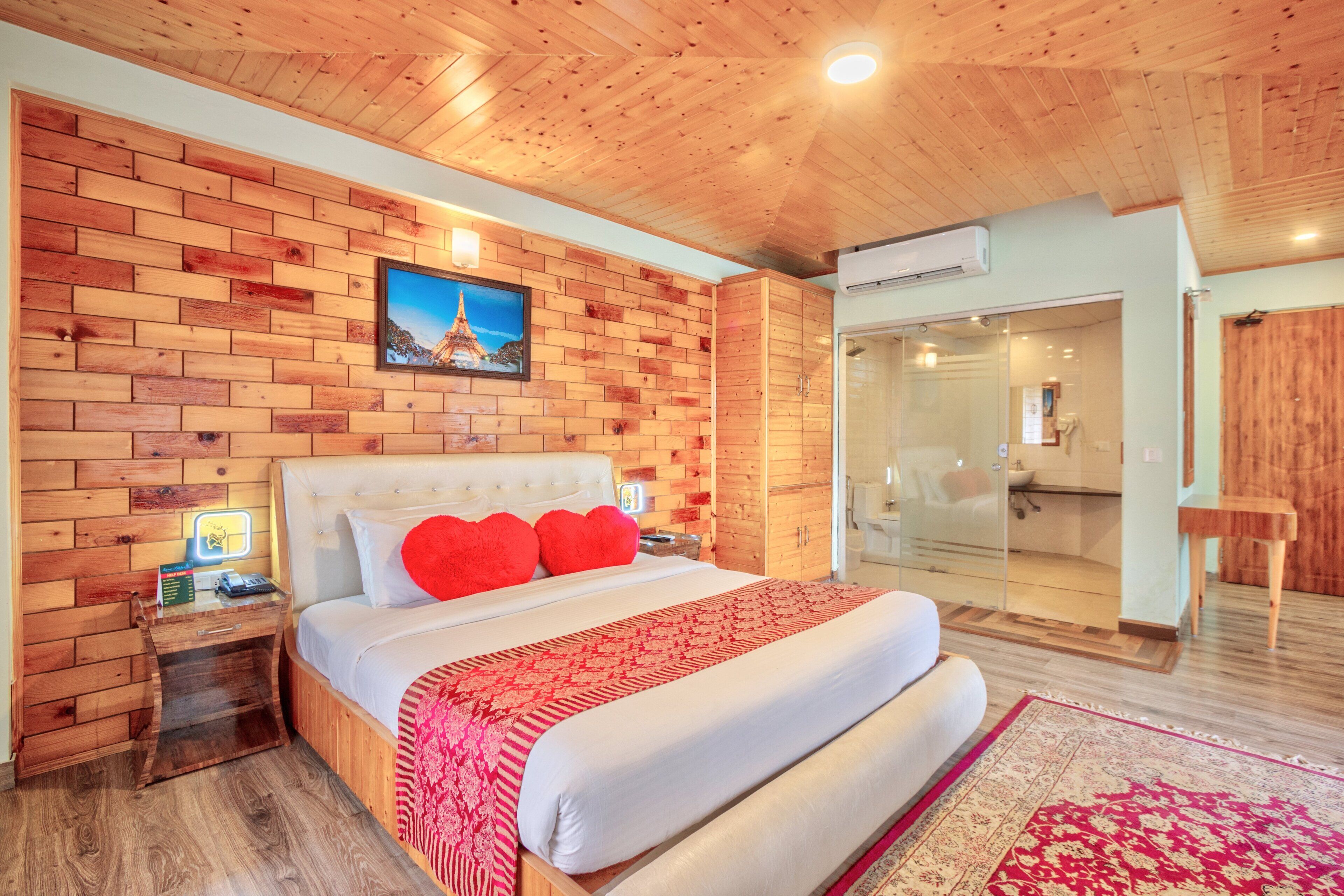 A wooden-paneled bedroom with a large bed, a nightstand, a glass shower enclosure, and a wooden wardrobe.