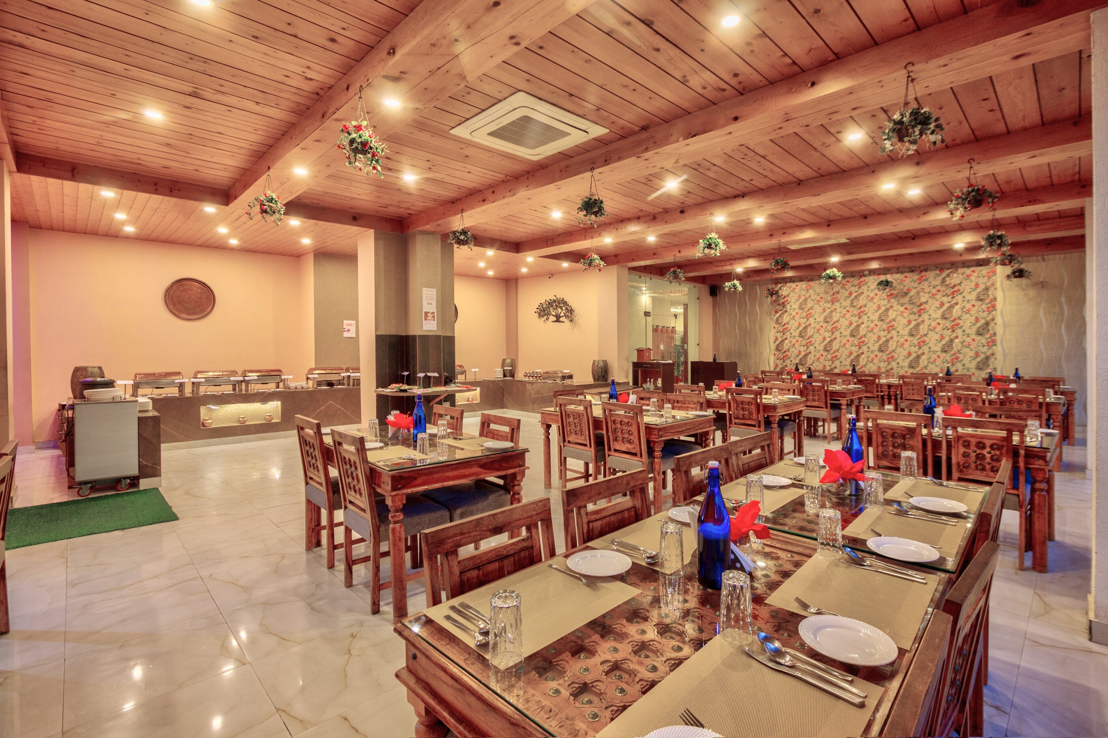 Un restaurant avec des tables et des chaises en bois, un espace buffet et un mur décoré de motifs.